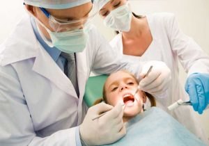 Image of dental checkup being given to little girl by dentist with assistant near by