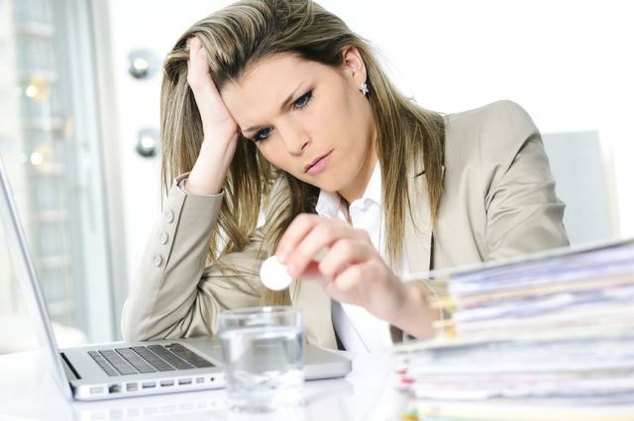 young woman stressed at work, taking an aspirin cahet